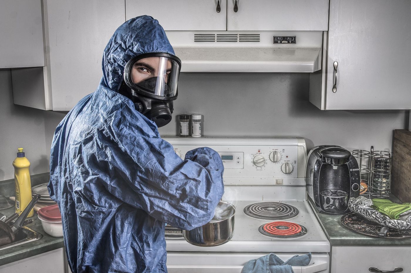 Personne en combinaison et masque de protection préparant un produit chimique dans une cuisine